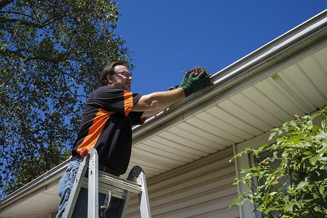 smiling worker fixing gutters on a residential home in Andover, CT